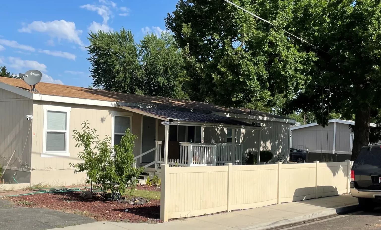 Resident home with a fenced yard and mature shade tree at Hampton Park MHC, an Elevation community in Boise, Idaho
